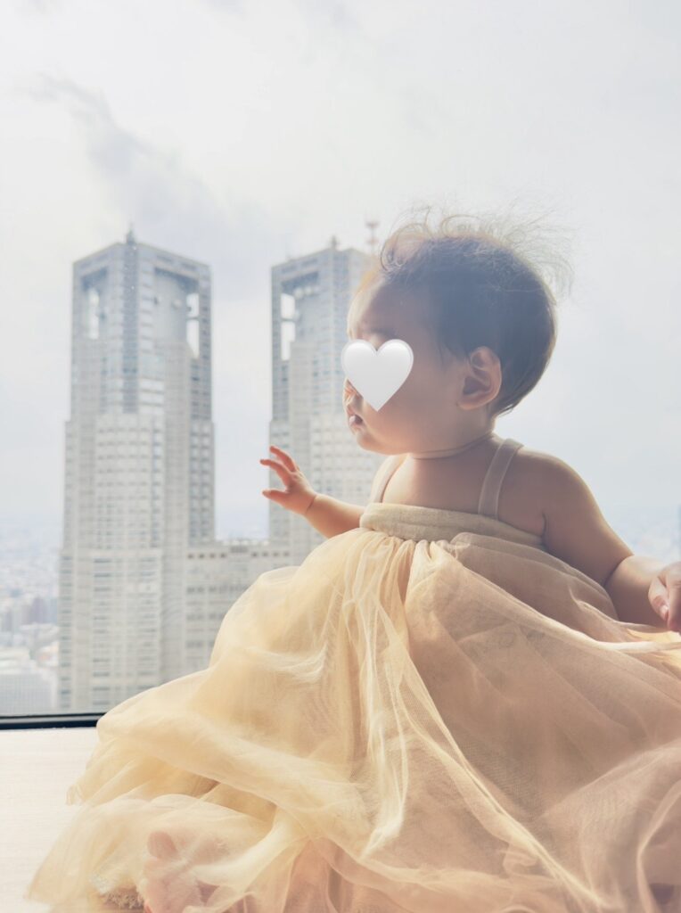 SKY PLAZA IBASHOの大きな窓辺に座る赤ちゃん。背景には新宿の高層ビル群が見える。