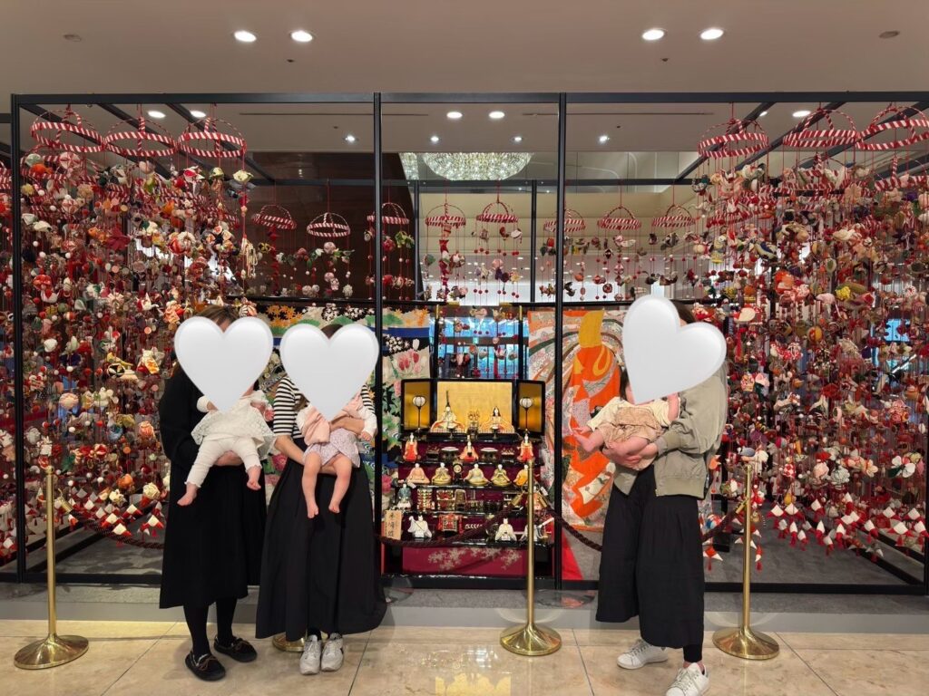 京王プラザホテル新宿の雛壇とつるし雛の前で、赤ちゃんを抱いた大人たちが並んで撮影している様子