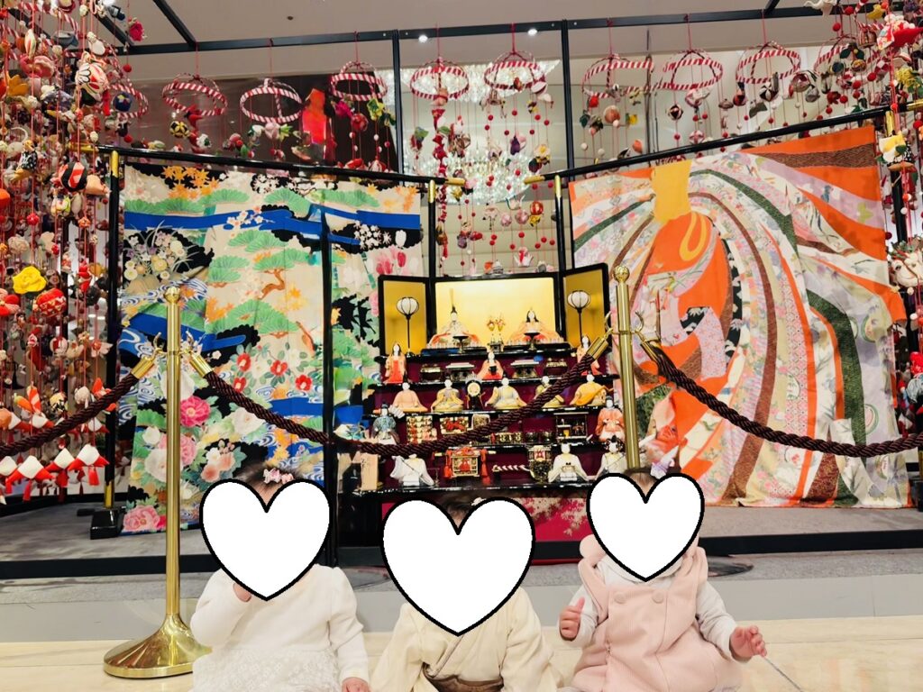 京王プラザホテル新宿のメインロビーに飾られた豪華な雛壇とつるし雛の前で、子どもたちが並んで座っている様子