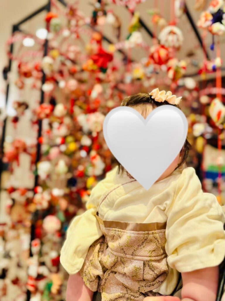 色とりどりのつるし雛の前で、和服を着た赤ちゃんが抱っこされている様子