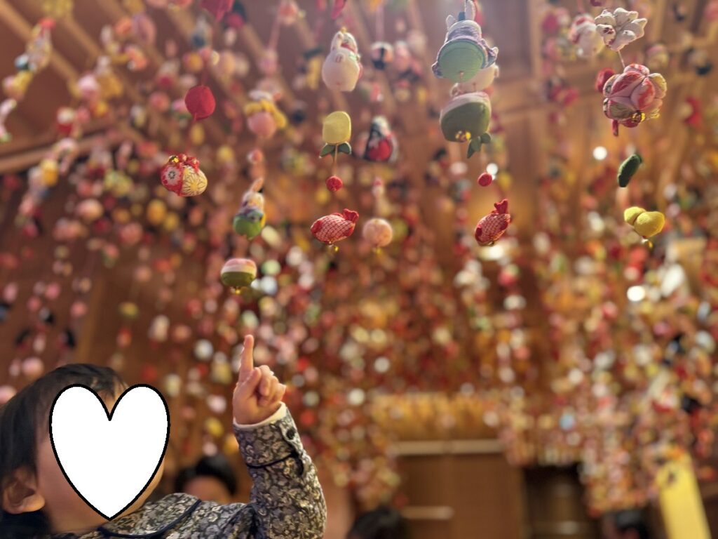 宗家 源 吉兆庵 銀座本店の天井いっぱいに飾られたつるし雛を指さして見上げる子ども。色とりどりの布細工が揺れる展示