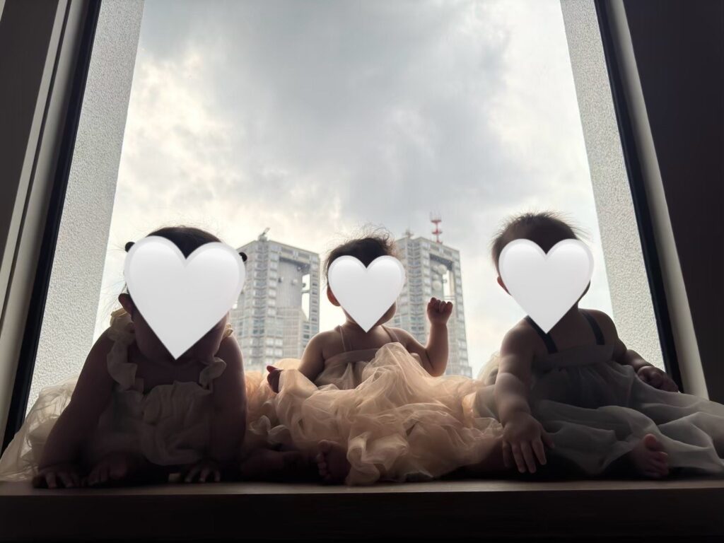 SKY PLAZA IBASHOの大きな窓辺に並んで座る赤ちゃん。背景には新宿の高層ビル群が見える。逆光で写真が暗くなってしまっている。