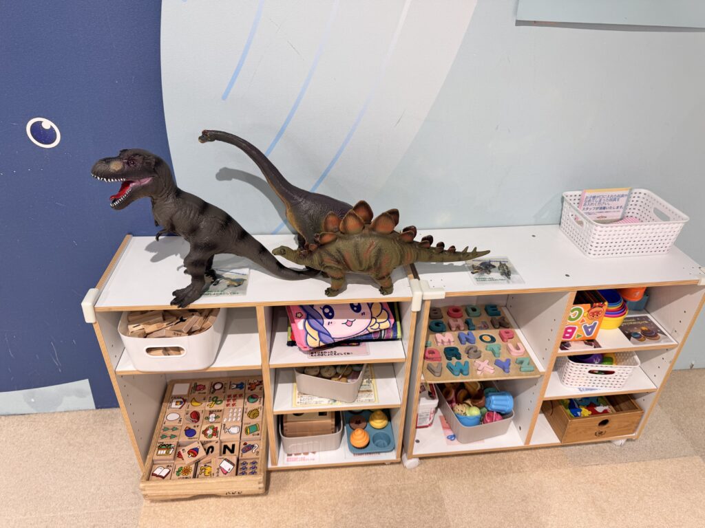 横浜アソビルのおもちゃ棚に並ぶ恐竜フィギュアや知育玩具の写真。